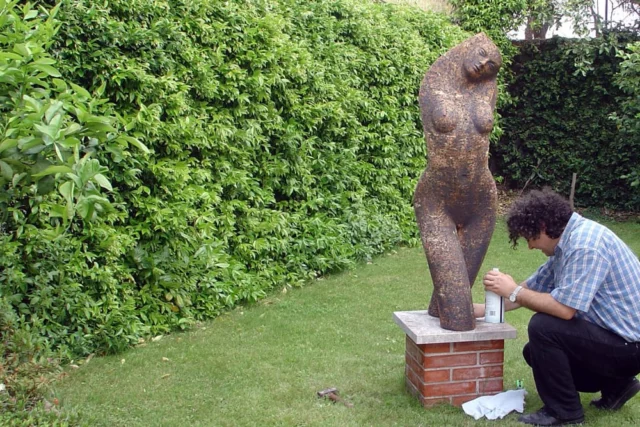lo scultore ylli plaka lucida la propria opera all'interno di un giardino. l'opera Ã¨ una figura femminile quasi a dimensione umana di gres